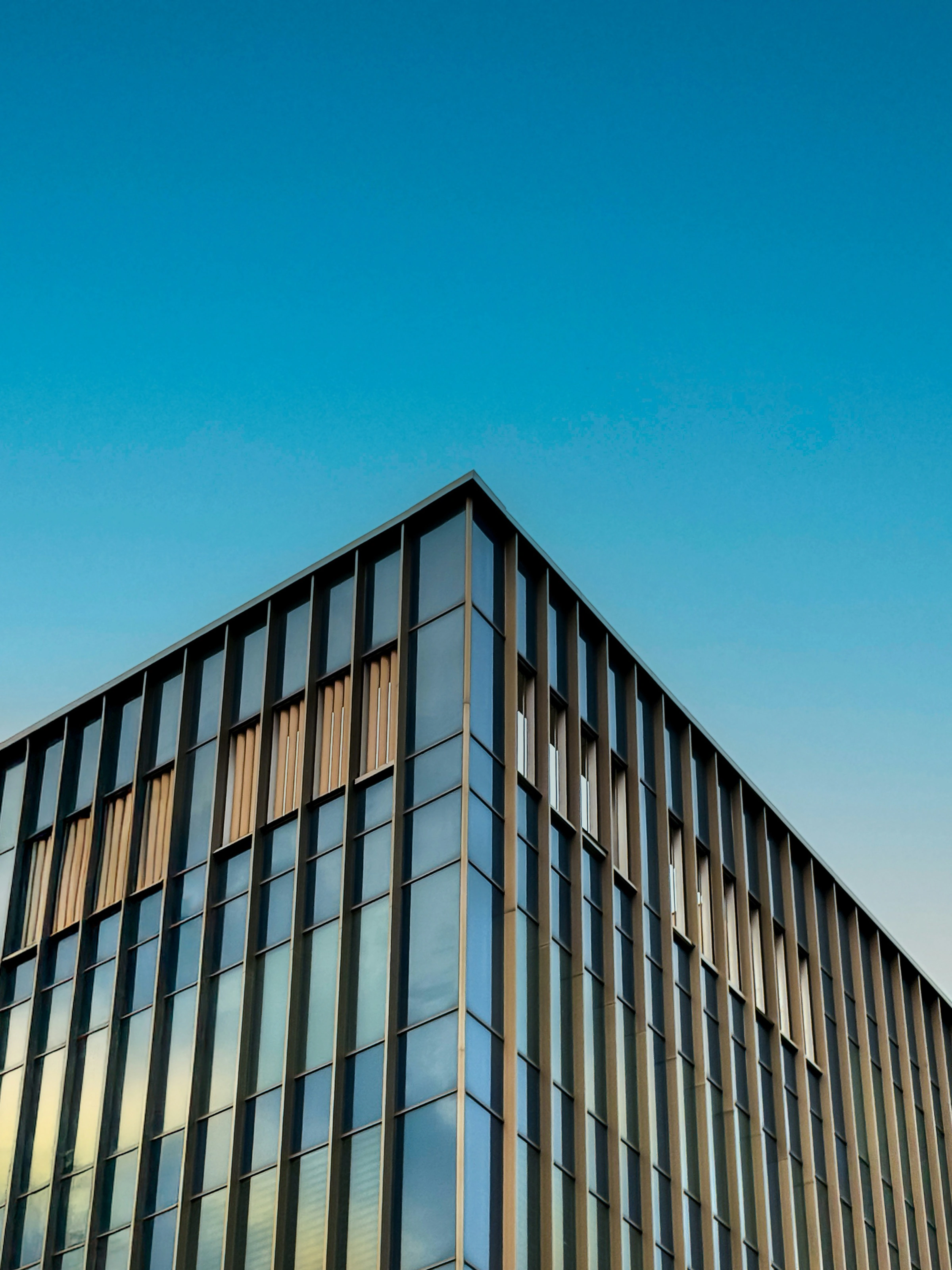 The corner of a glass and bronze facade with slender vertical fins against a clear blue sky