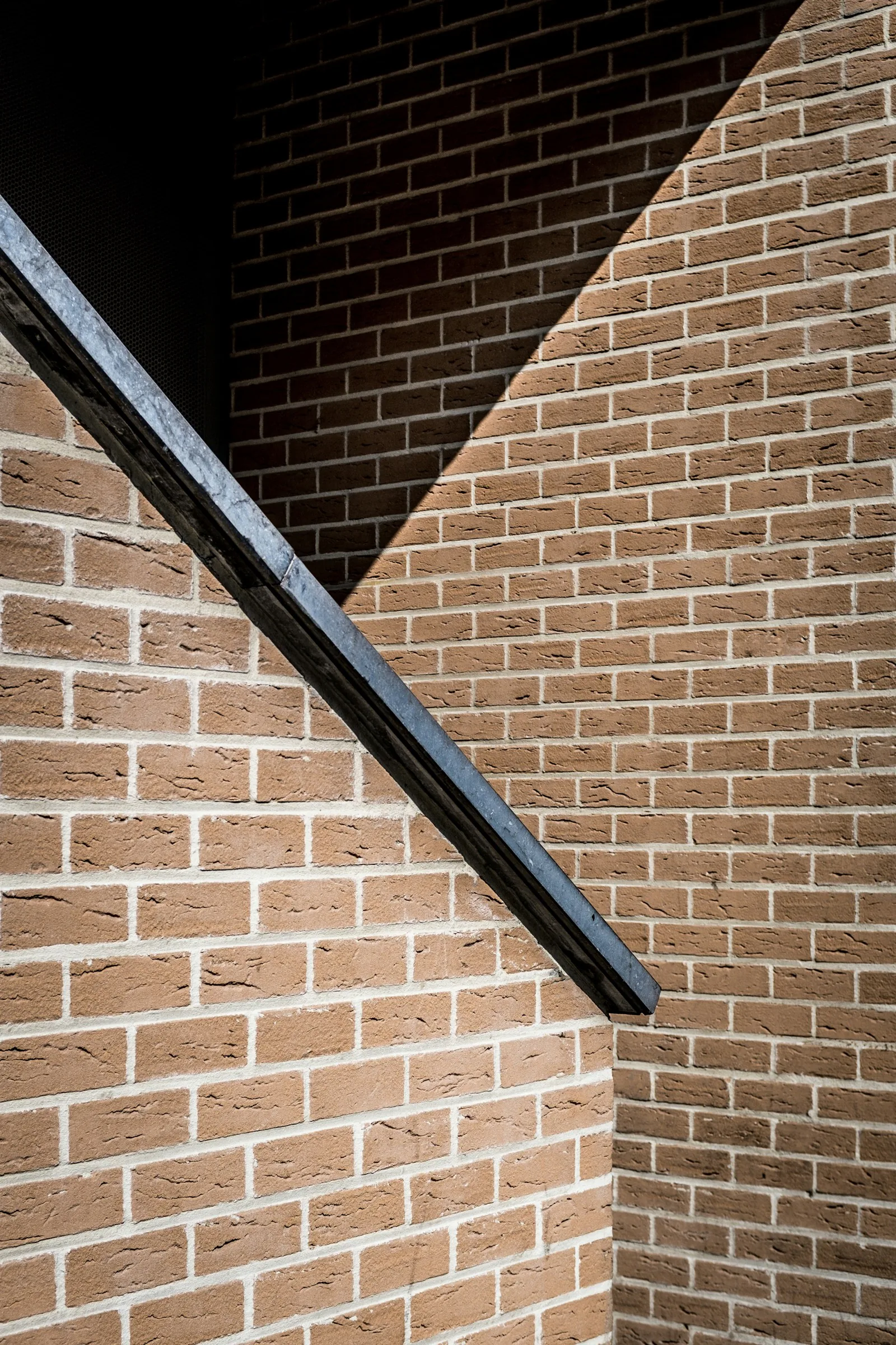 A brick wall crossed by a dark steel handrail