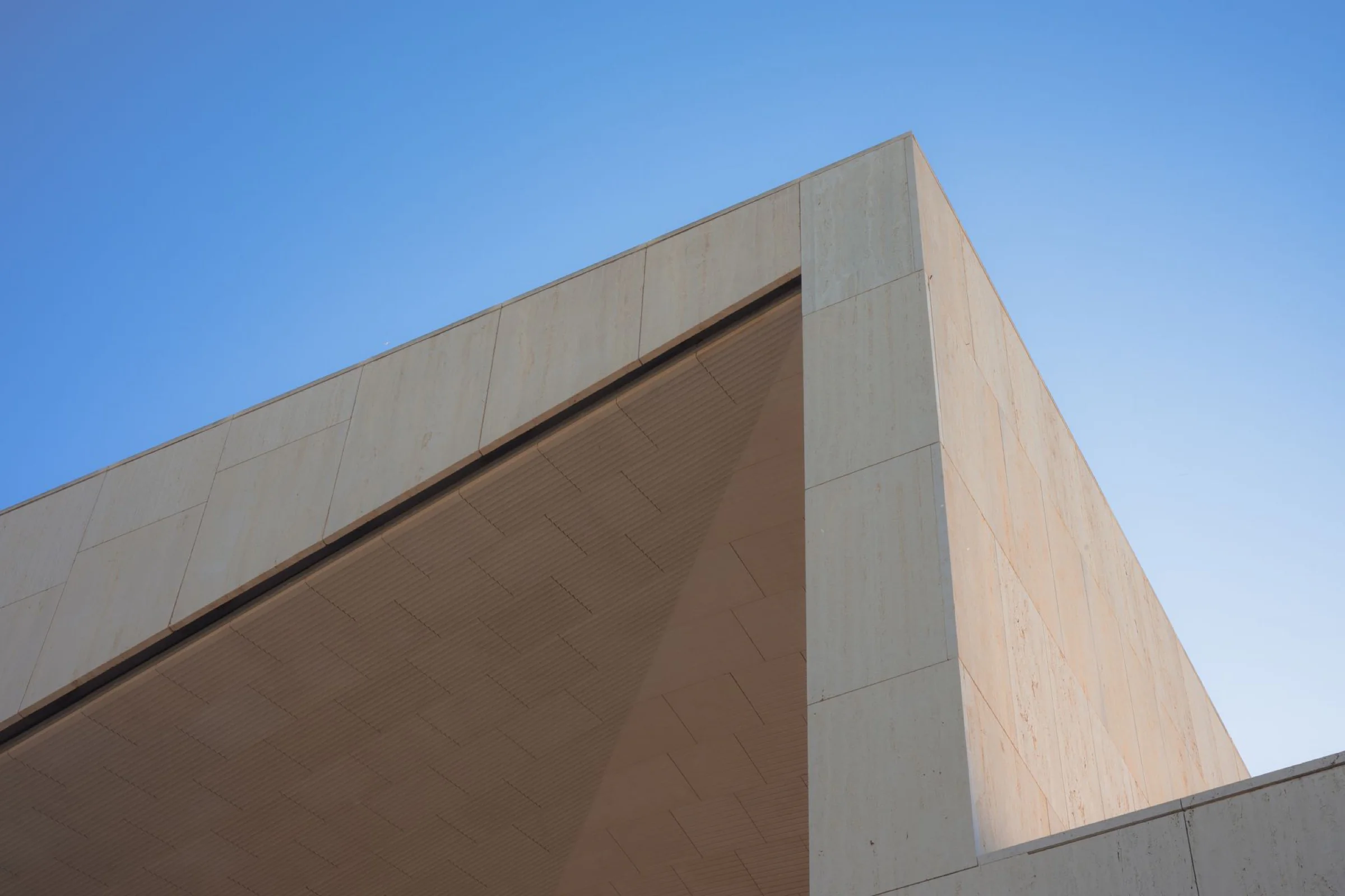 A sharp corner of pale travertine cladding against a clear blue sky