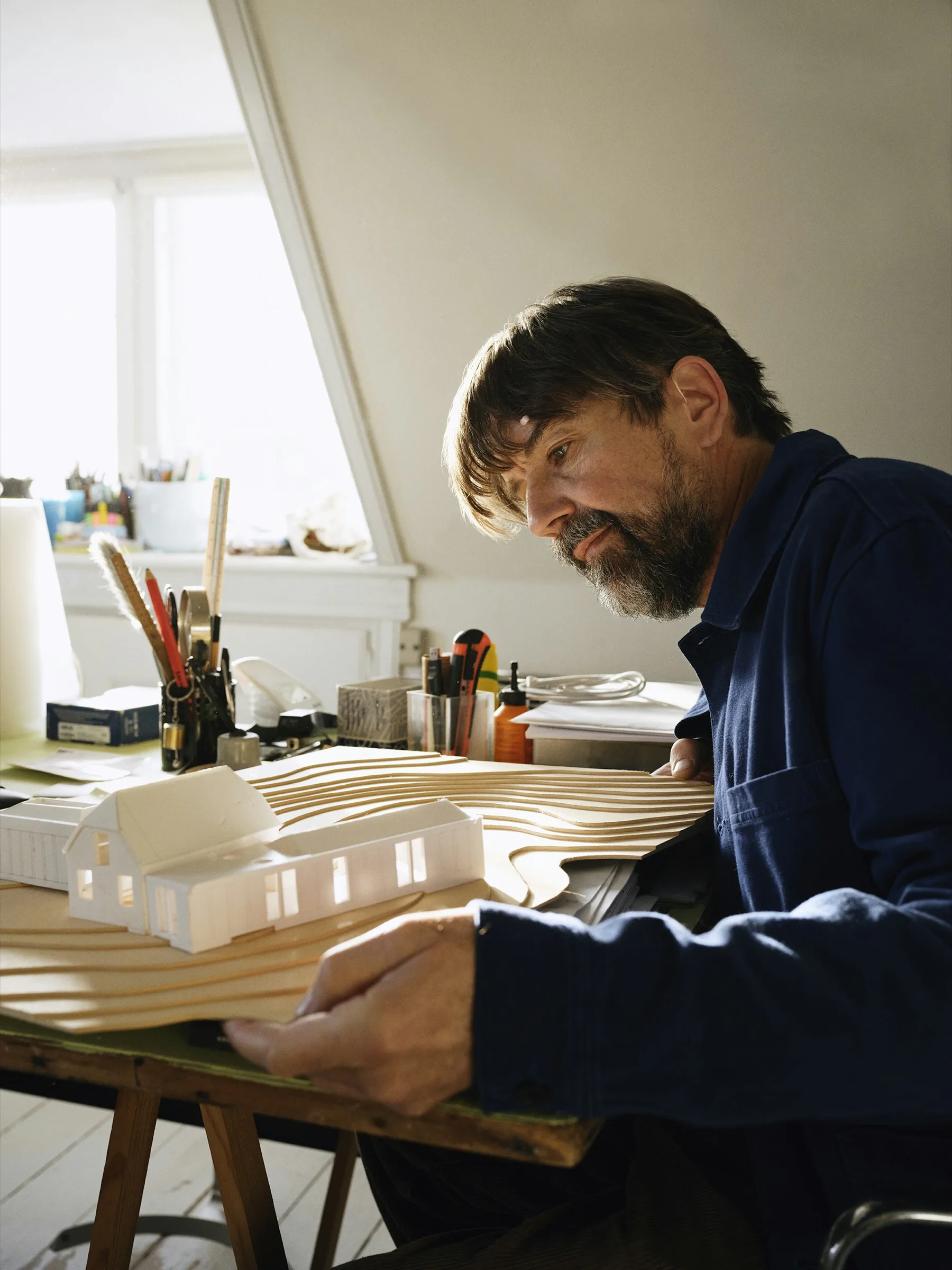 Architect working on a white model at a desk covered in tools